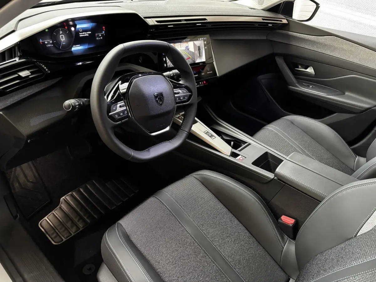Vue intérieure côté conducteur du Peugeot 308 Hybrid 145 e-DCS6 Allure 2025, volant cuir multifonctions et écran tactile central.