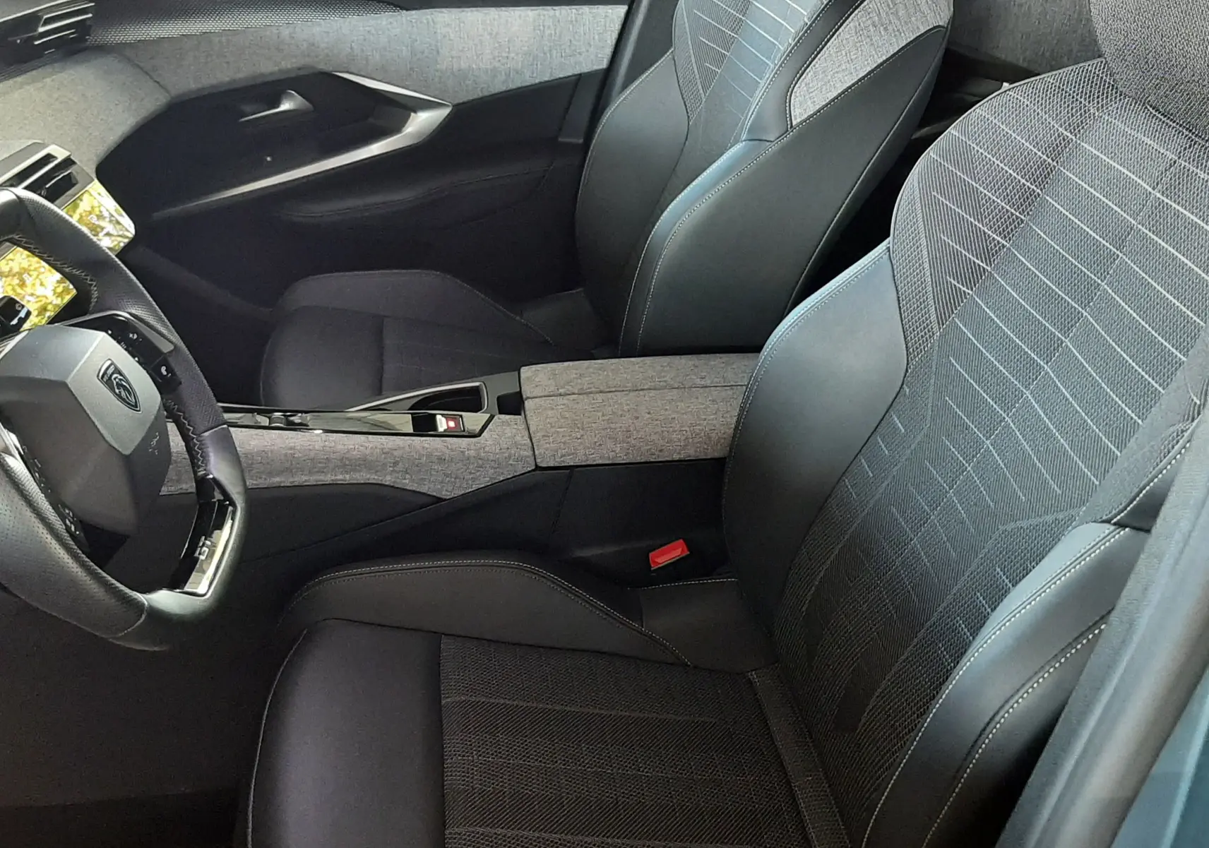 Vue intérieure côté conducteur du Peugeot 3008 2025, sièges tissu et cuir noir avec logo Peugeot brodé sur appuie-tête.