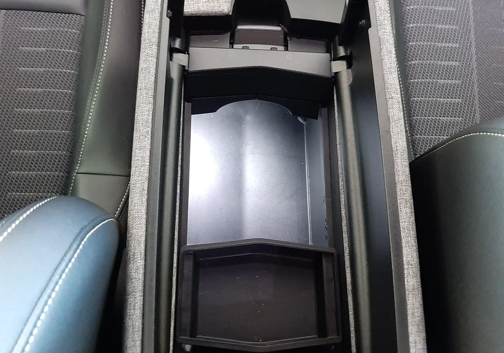 Vue plongeante sur le rangement central ouvert du Peugeot 3008 1.2 Hybrid 145ch GT, intérieur noir avec accoudoir bleu Ingaro.