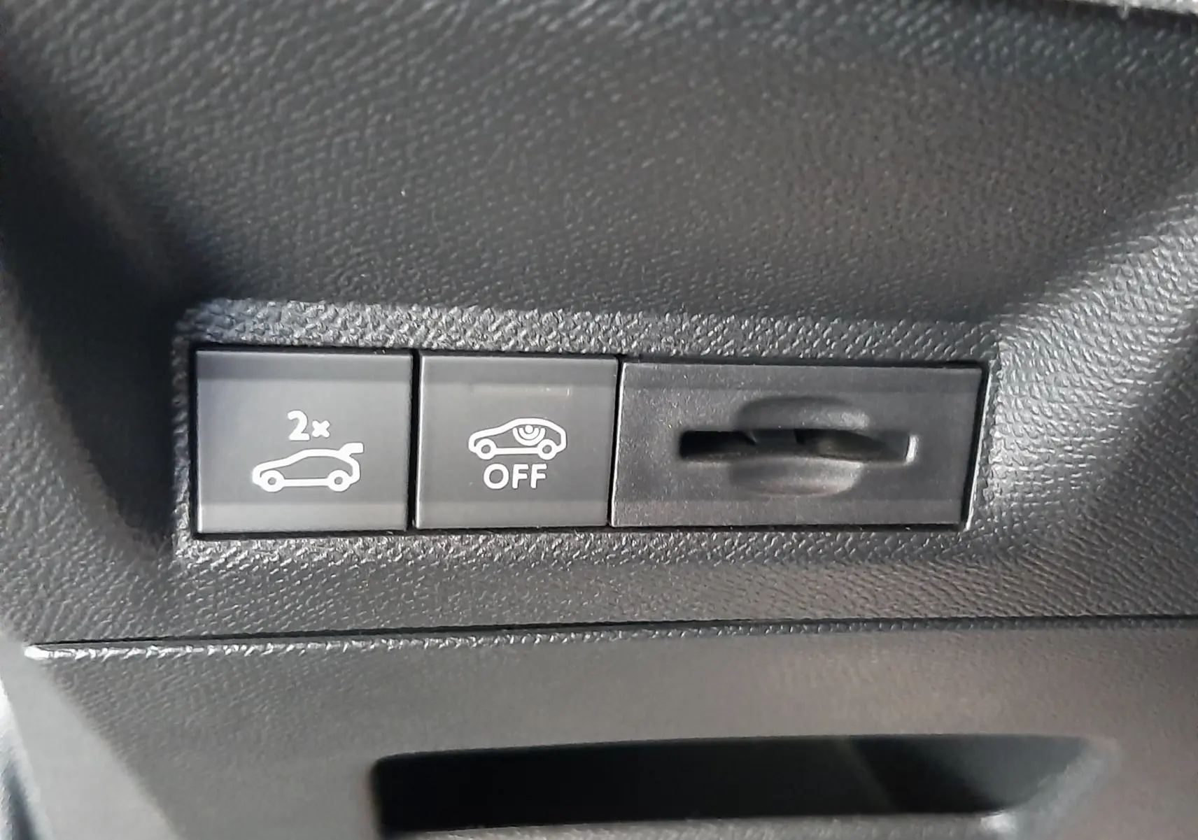Gros plan sur les boutons de commande intérieurs noirs du Peugeot 3008 1.2 Hybrid bleu Ingaro, avec symboles d'ouverture de coffre et désactivation d'assistance.