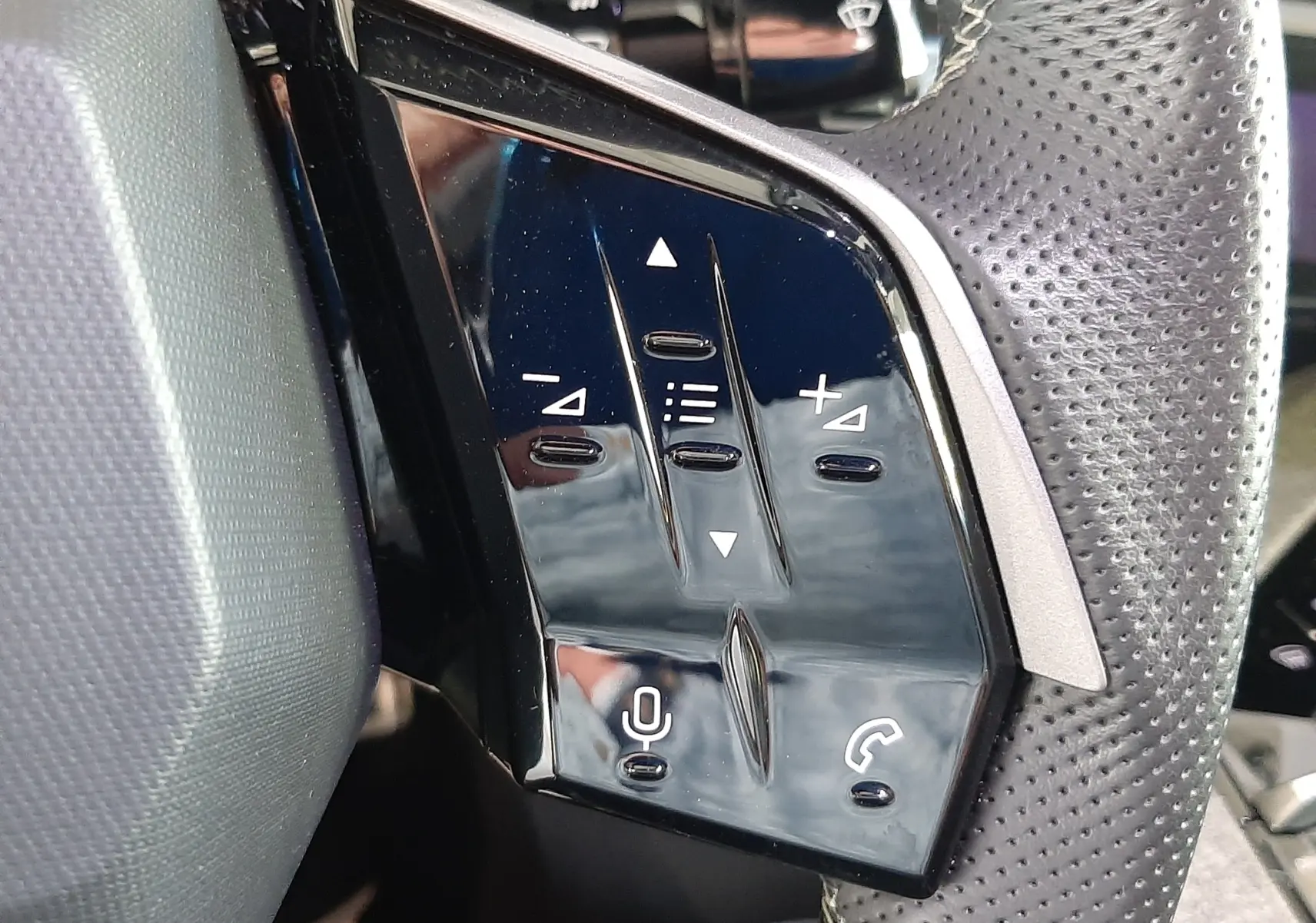 Gros plan sur les commandes tactiles noires du volant perforé du Peugeot 3008 Hybrid 2025, avec boutons de volume et appel.