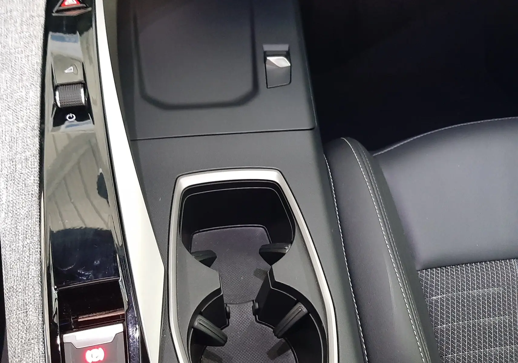 Vue rapprochée de la console centrale du Peugeot 3008 1.2 Hybrid 145ch GT 2025, avec porte-gobelets et bouton frein à main électrique.