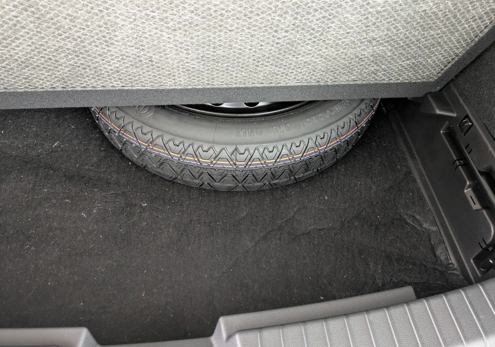 Gros plan sur la roue de secours dans le coffre du Dacia Bigster Hybrid 155 Extreme, tapis noir visible.