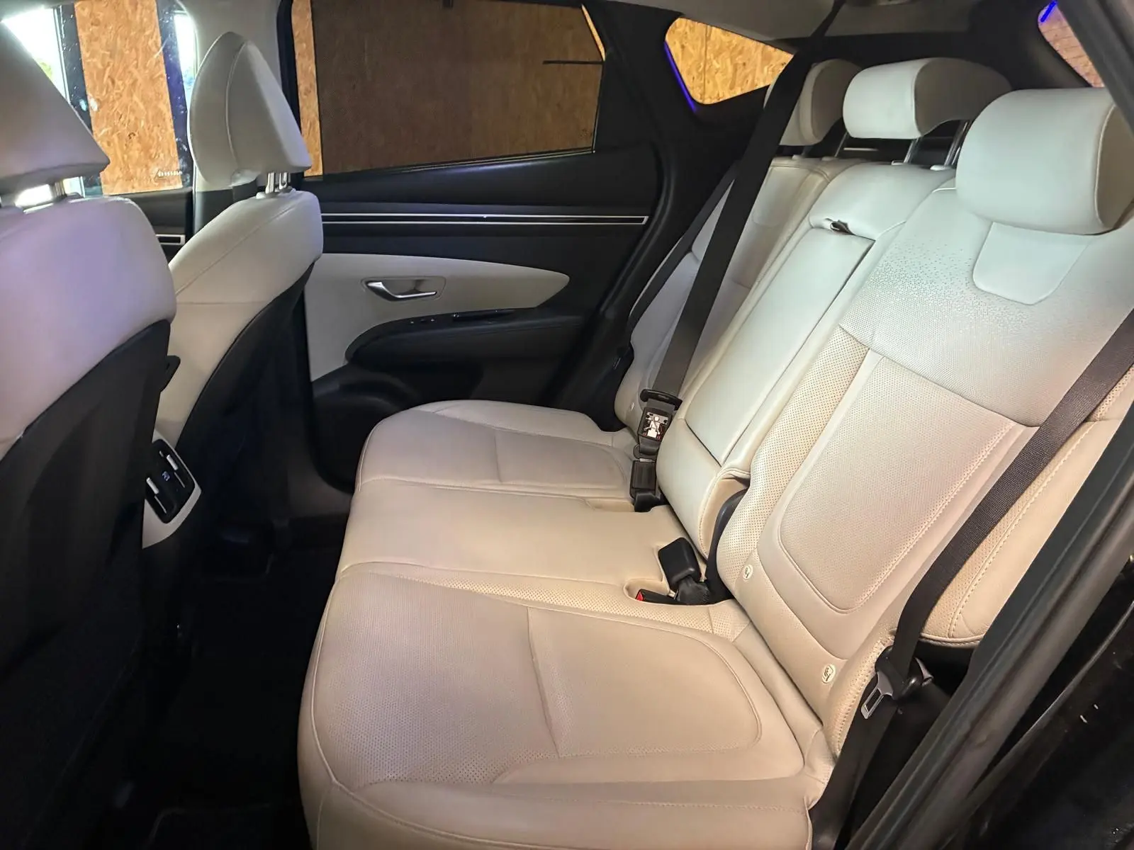 Vue intérieure côté gauche des sièges arrière en cuir beige du Hyundai Tucson noir 2022, avec ceinture de sécurité visible.