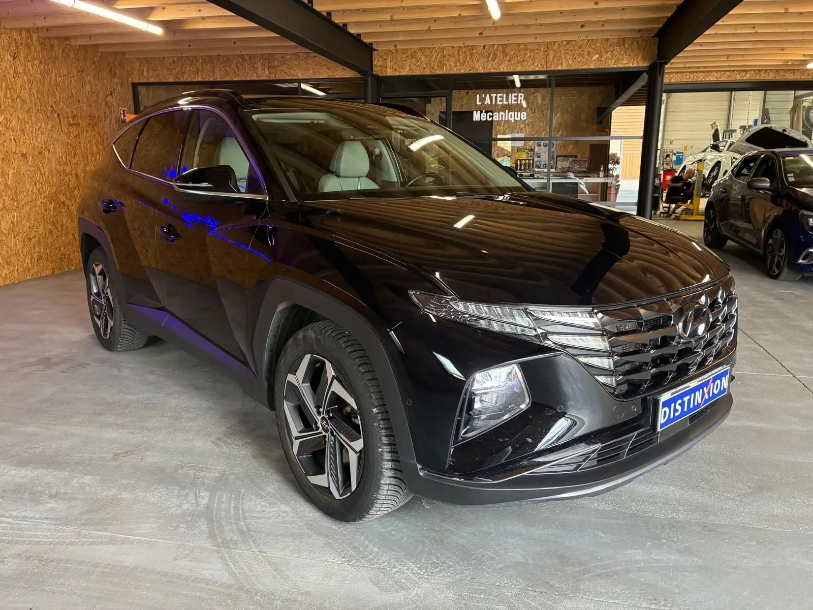 Vue 3/4 avant droite du Hyundai Tucson noir 2022, soulignant sa calandre distinctive et ses jantes modernes en intérieur d'atelier.