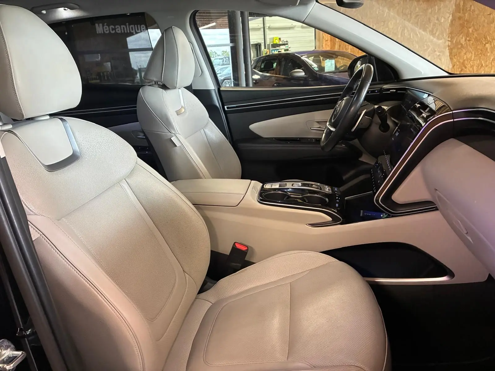 Vue intérieure côté conducteur du Hyundai Tucson 1.6 T-GDI Hybrid 230 Executive 2022 avec sièges cuir beige et tableau de bord noir.