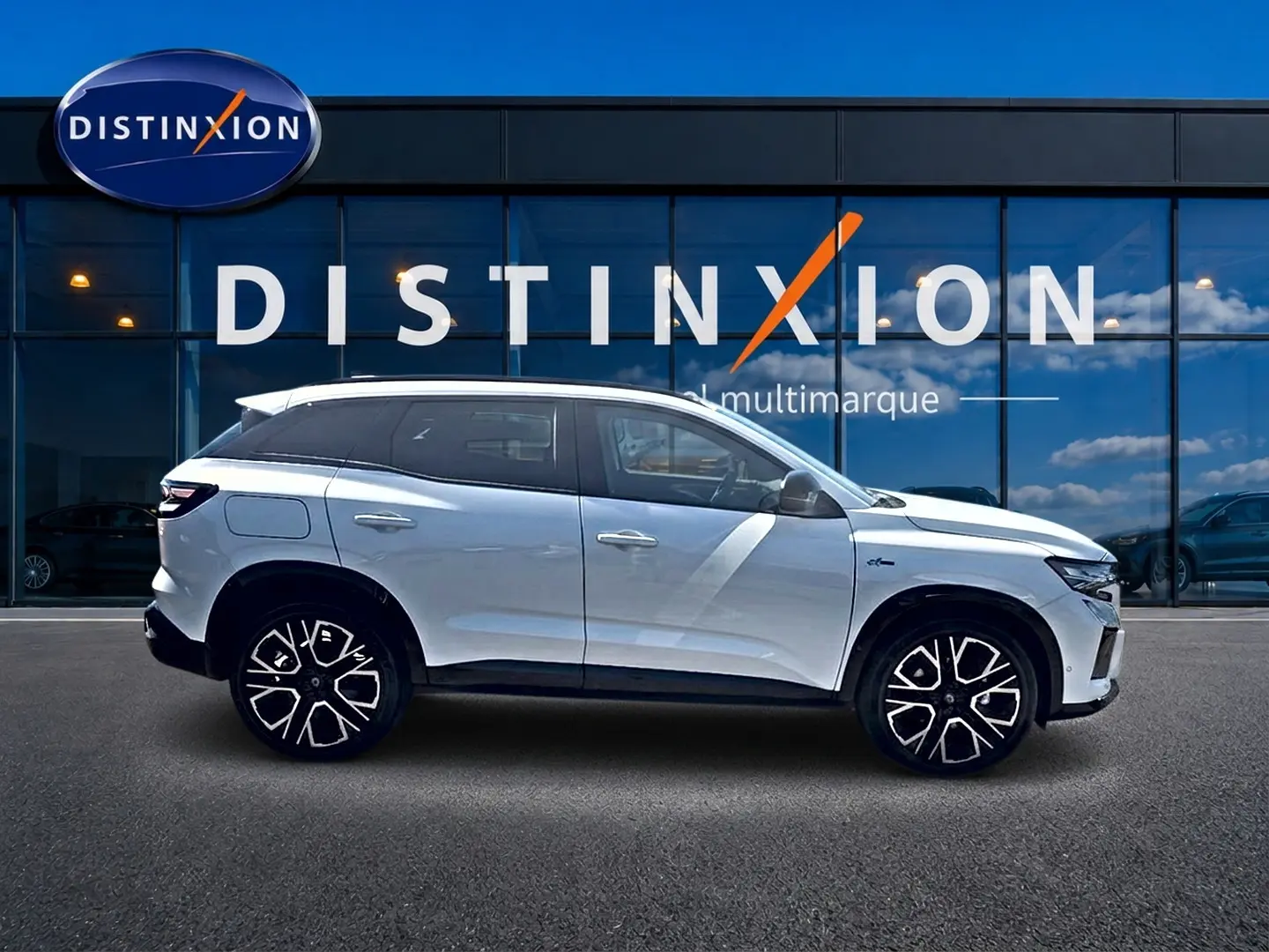 Profil droit d’un Renault Austral blanc nacré 2026 avec jantes alu noires et toit noir devant une vitrine Distinxion.