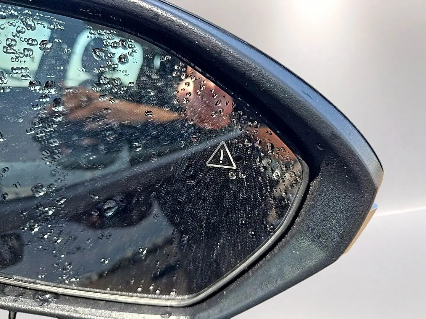 Gros plan sur le rétroviseur droit noir du Hyundai Tucson 2026 avec gouttes d'eau et symbole d'alerte visible.