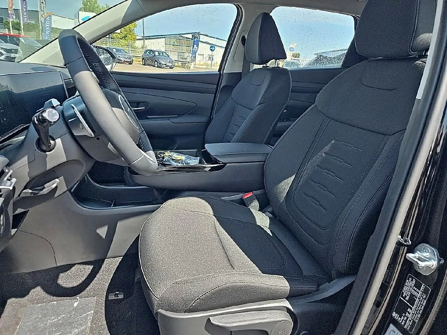 Vue intérieure côté conducteur du Hyundai Tucson 2026 noir, sièges tissu noir et volant cuir multifonction.