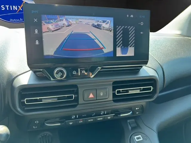 Écran central du Citroën Berlingo 2025 noir montrant la caméra de recul avec guidage dynamique sur parking extérieur.