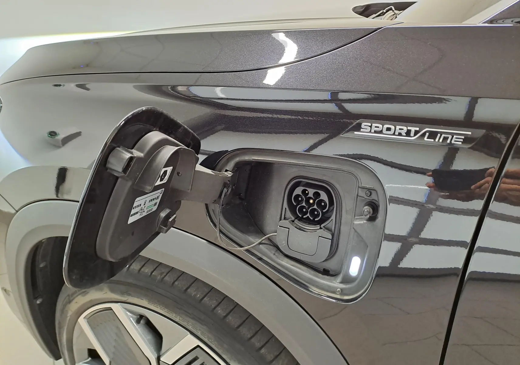 Prise de recharge ouverte côté gauche d’un Skoda Kodiaq noir nacré Sportline, avec jante alliage visible.