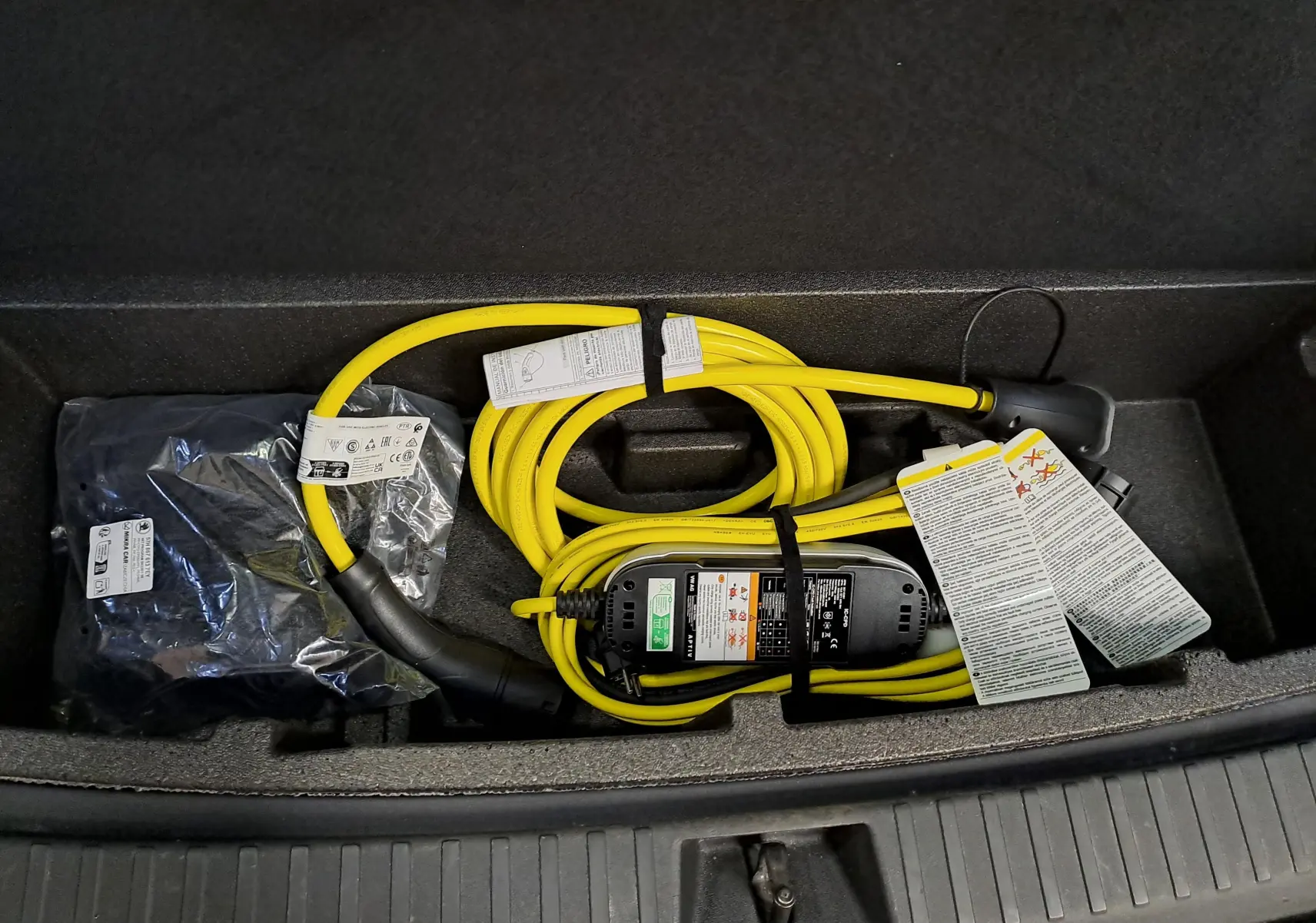 Câble de recharge jaune enroulé dans le coffre d'un Skoda Kodiaq noir Magic nacré, vue de dessus.