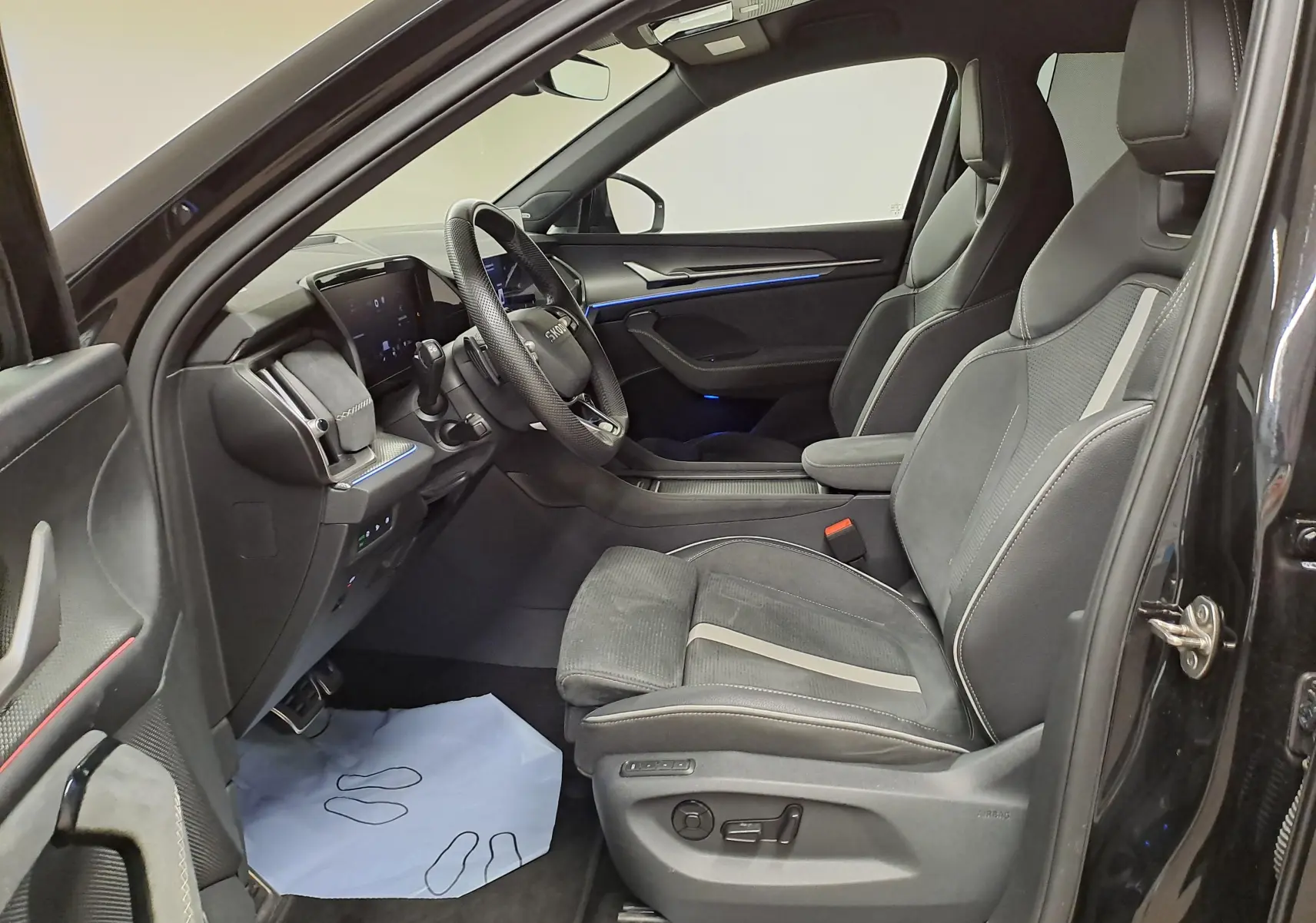 Intérieur côté conducteur du Skoda Kodiaq noir nacré 2025, sièges sport en cuir et tableau de bord avec éclairage bleu.