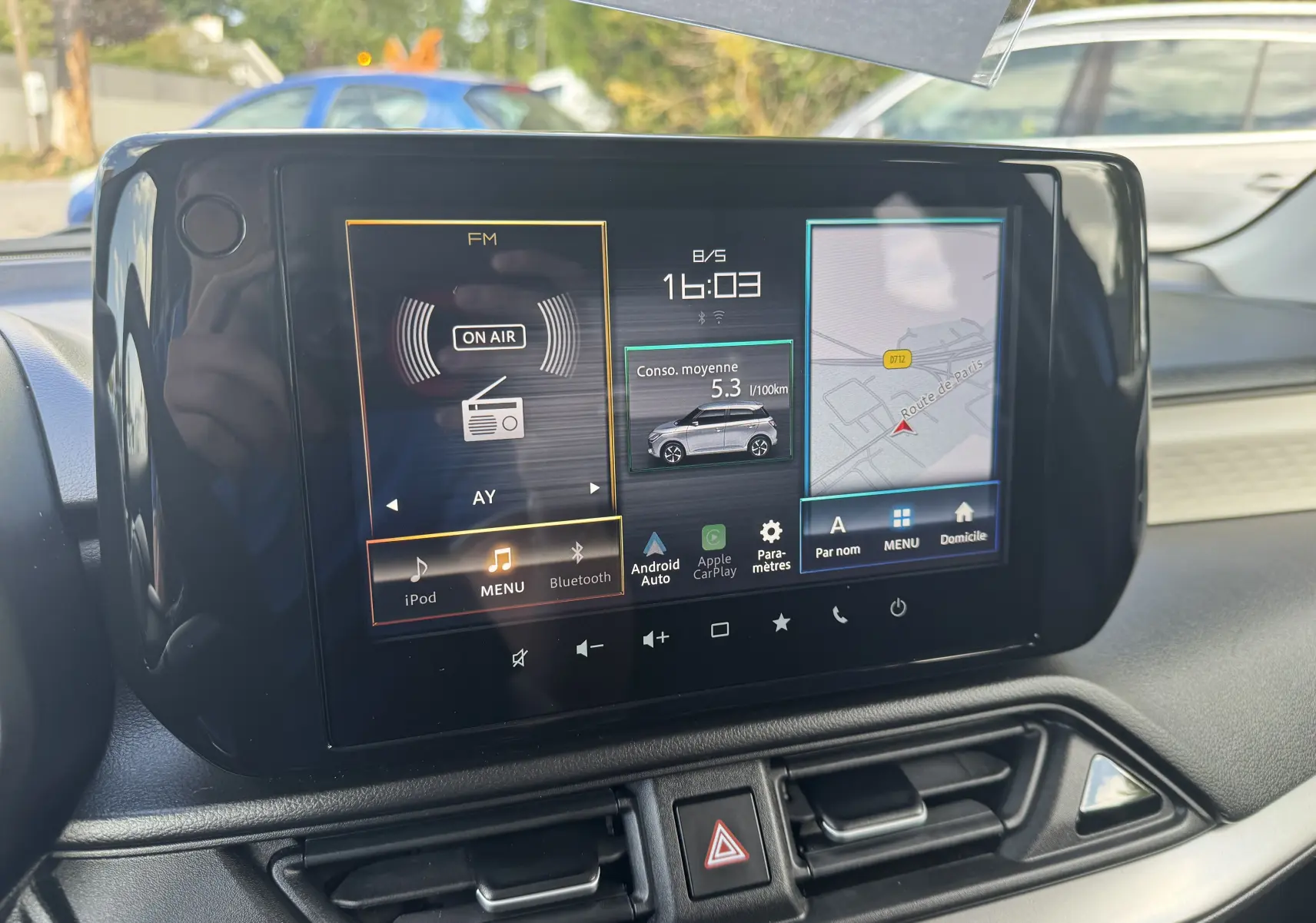 Écran tactile central de la Suzuki Swift 1.2 Pack Hybrid 2024 affichant radio, consommation moyenne et navigation.