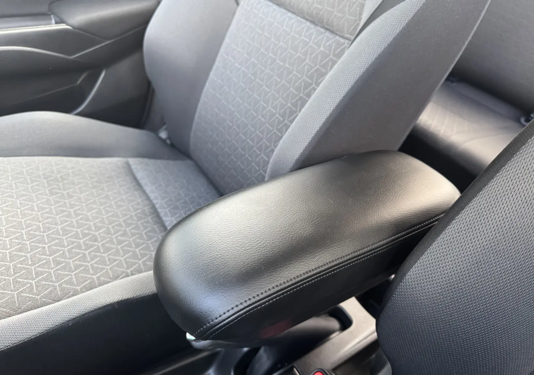 Vue rapprochée de l'accoudoir central noir et des sièges gris à motifs géométriques dans la Suzuki Swift 1.2 Pack Hybrid 2024.