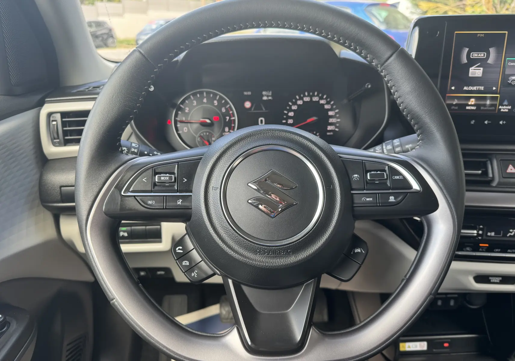 Vue centrée sur le volant noir de la Suzuki Swift 1.2 Pack Hybrid 2024 avec tableau de bord et écran multimédia en arrière-plan.
