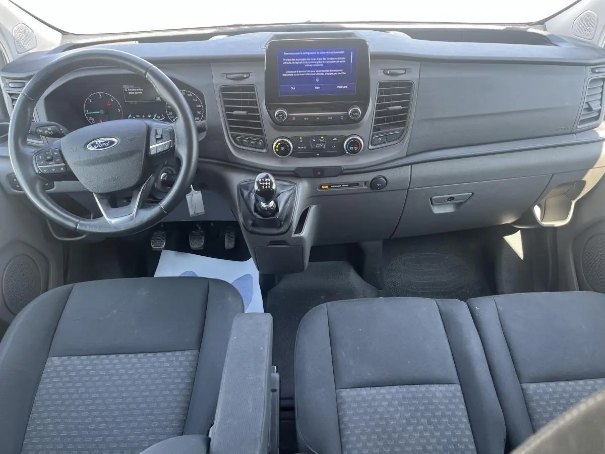 Vue intérieure avant du Ford Transit Custom blanc 2021, tableau de bord avec écran tactile et volant multifonction.