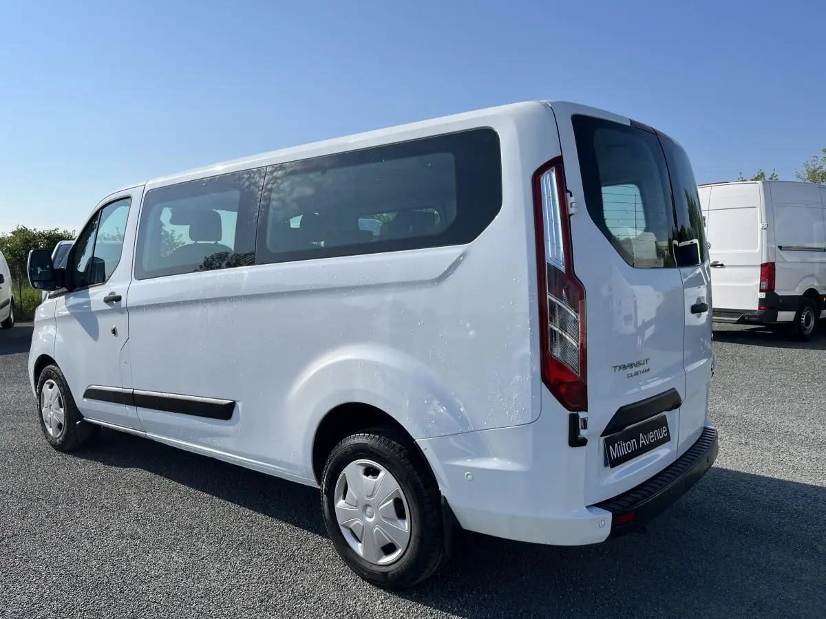 Vue 3/4 arrière droite du Ford Transit Custom Kombi blanc avec vitres latérales teintées et hayon vitré.