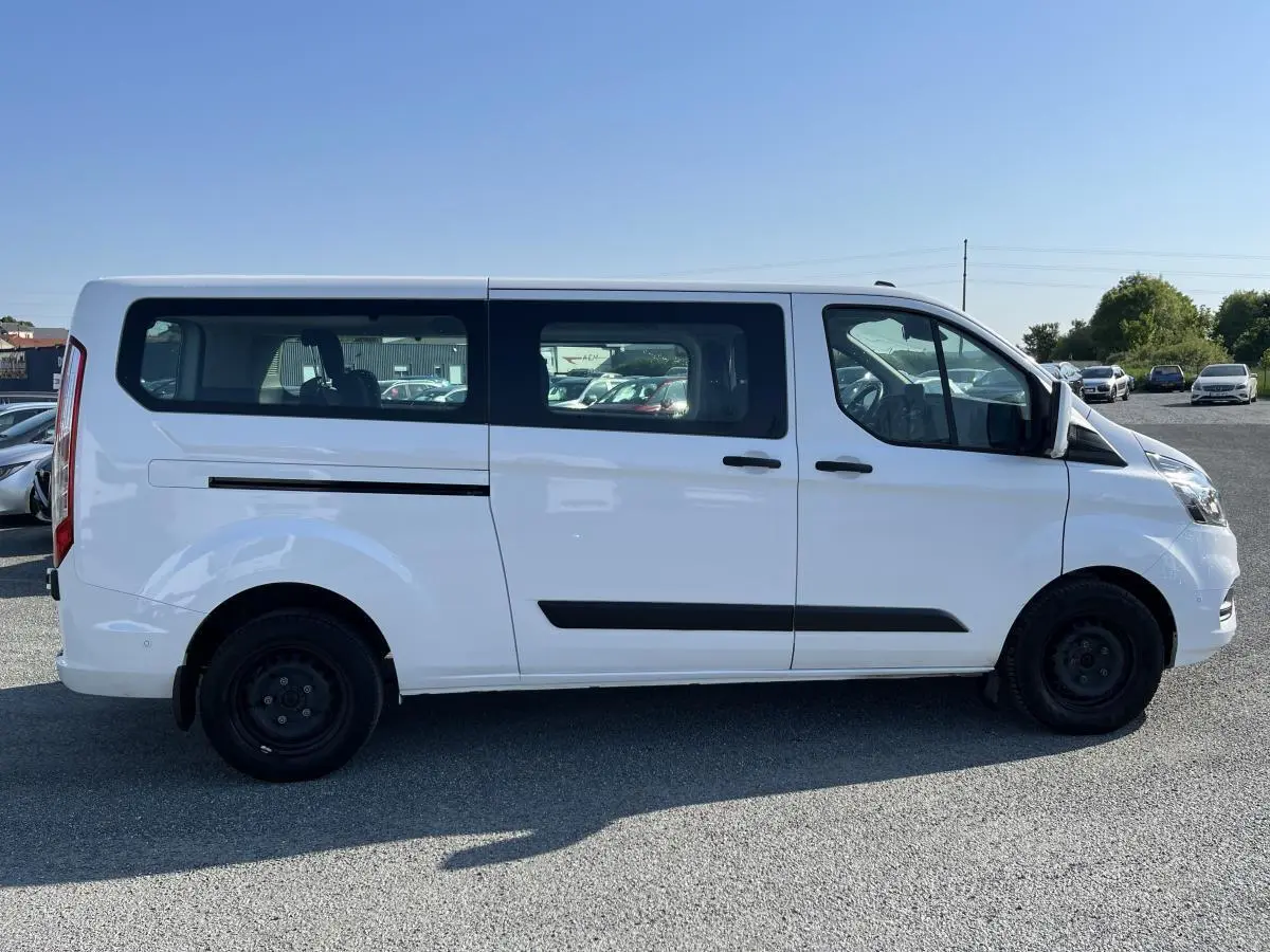 Profil côté droit d'un Ford Transit Custom Kombi blanc, avec vitres latérales teintées et jantes acier noires.
