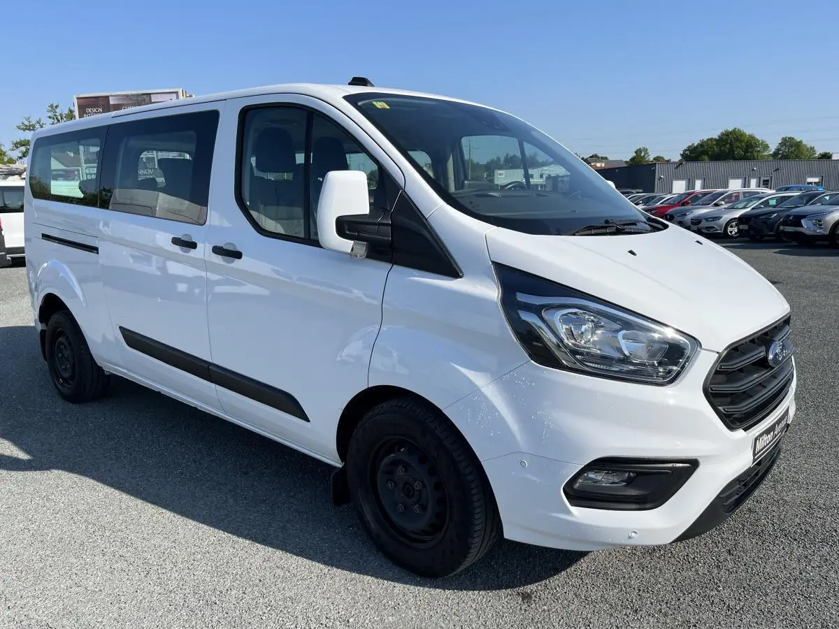 Vue 3/4 avant droite d'un Ford Transit Custom Kombi blanc avec calandre noire et jantes acier noires.