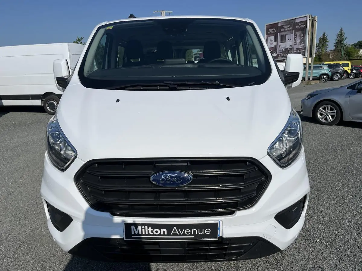 Vue frontale d'un Ford Transit Custom Kombi blanc avec calandre noire et plaque Milton Avenue visible.