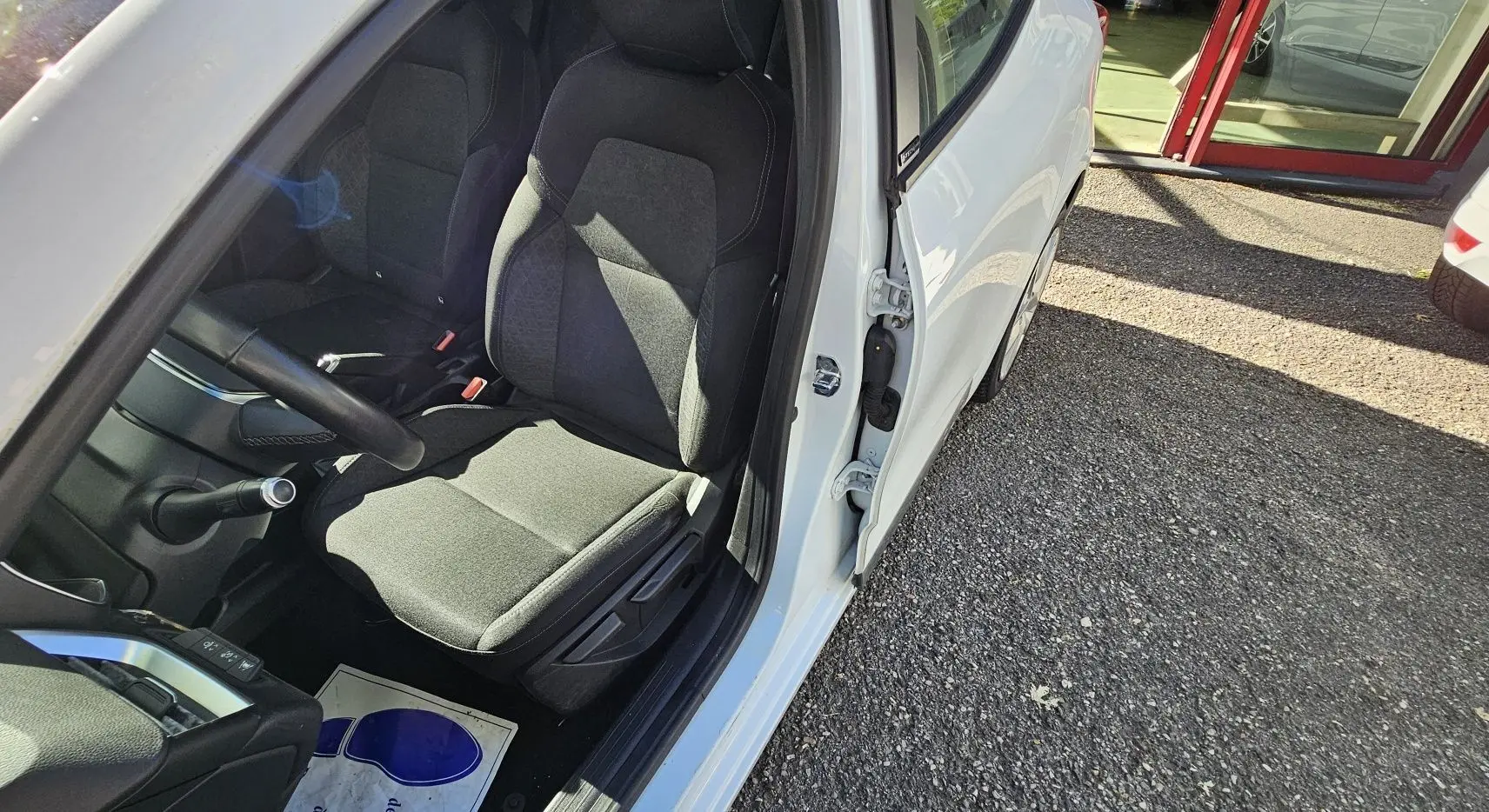 Vue intérieure côté conducteur d'une Renault Clio blanche glacier 2021, sièges noirs en tissu et tableau de bord visible.