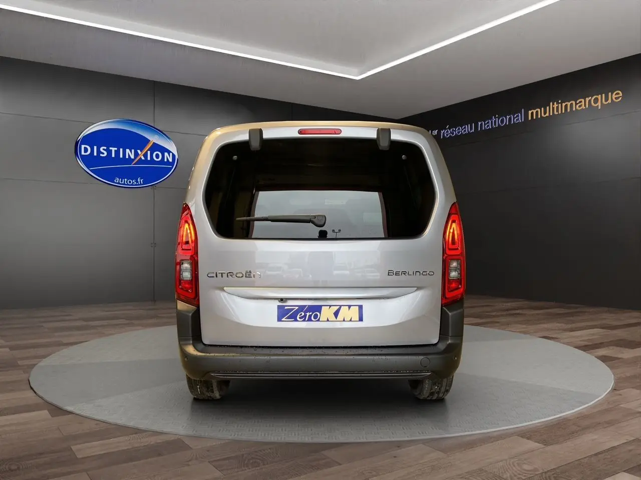 Vue arrière du Citroën Berlingo gris Artense 2025 avec hayon et feux arrière allumés en intérieur showroom.