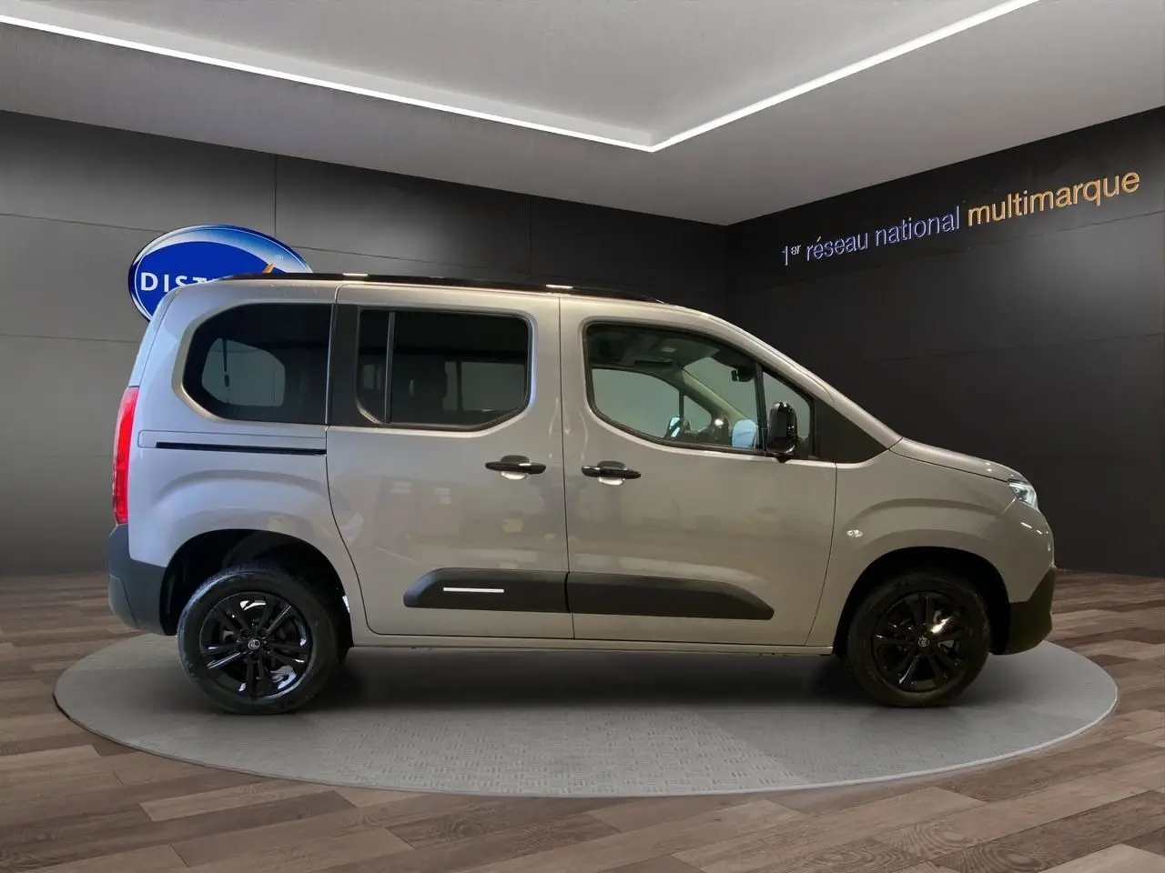 Profil droit du Citroën Berlingo gris Artense avec jantes noires et portes coulissantes visibles en intérieur showroom.