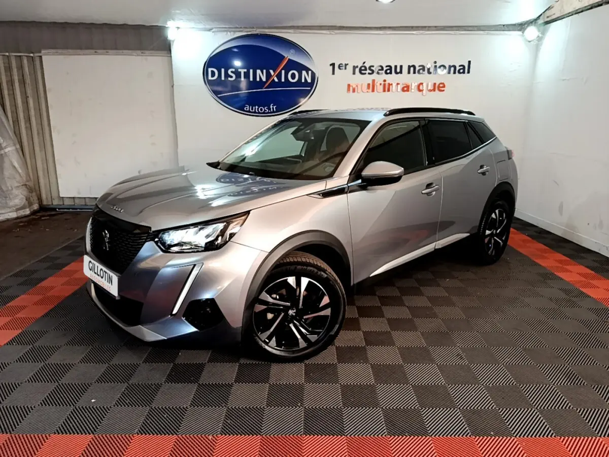 Peugeot 2008 gris clair en 3/4 avant droit, avec jantes noires et toit noir dans un showroom intérieur.