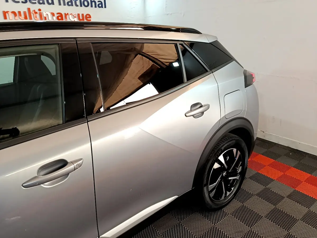Profil arrière droit d'un Peugeot 2008 gris clair avec jantes noires et toit noir contrasté en intérieur showroom.
