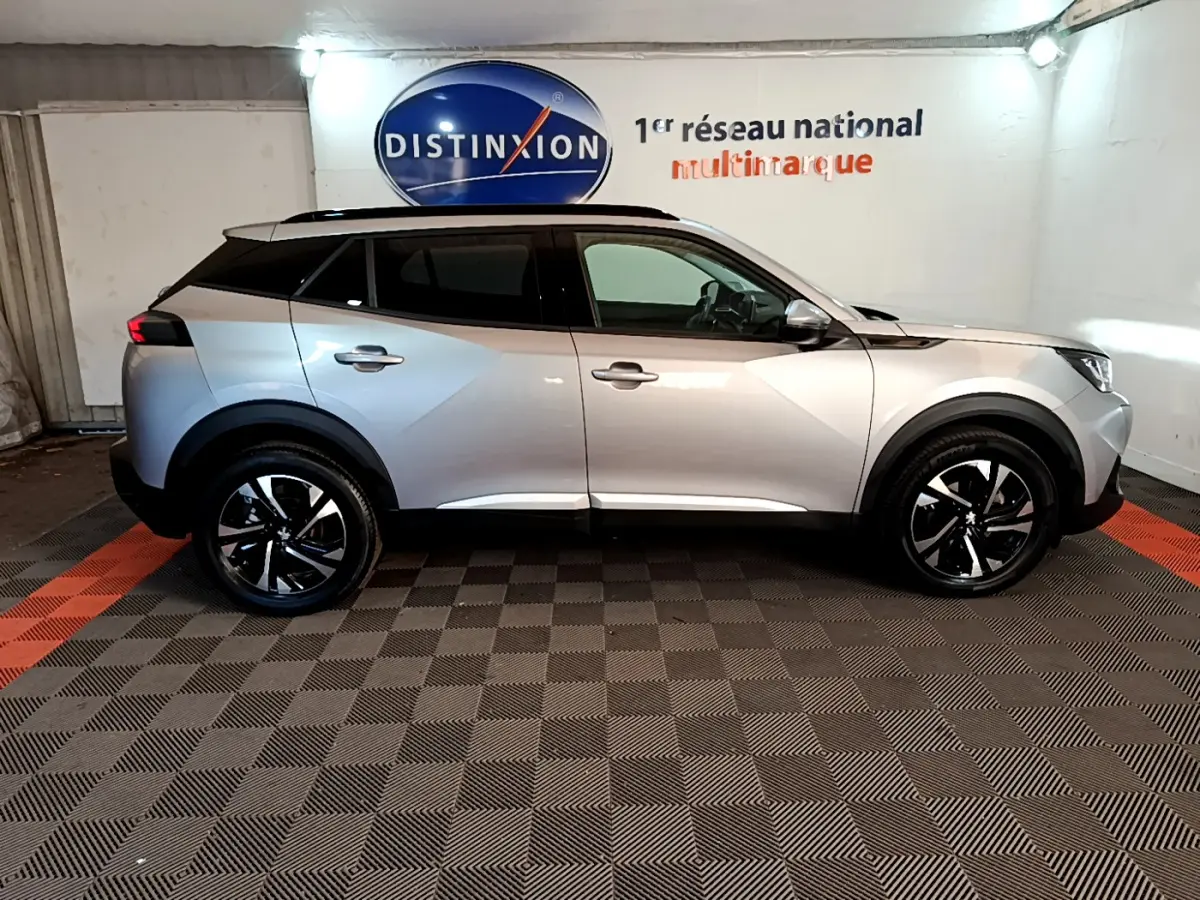Peugeot 2008 gris clair vue de profil côté gauche, avec jantes noires et toit panoramique en intérieur showroom.