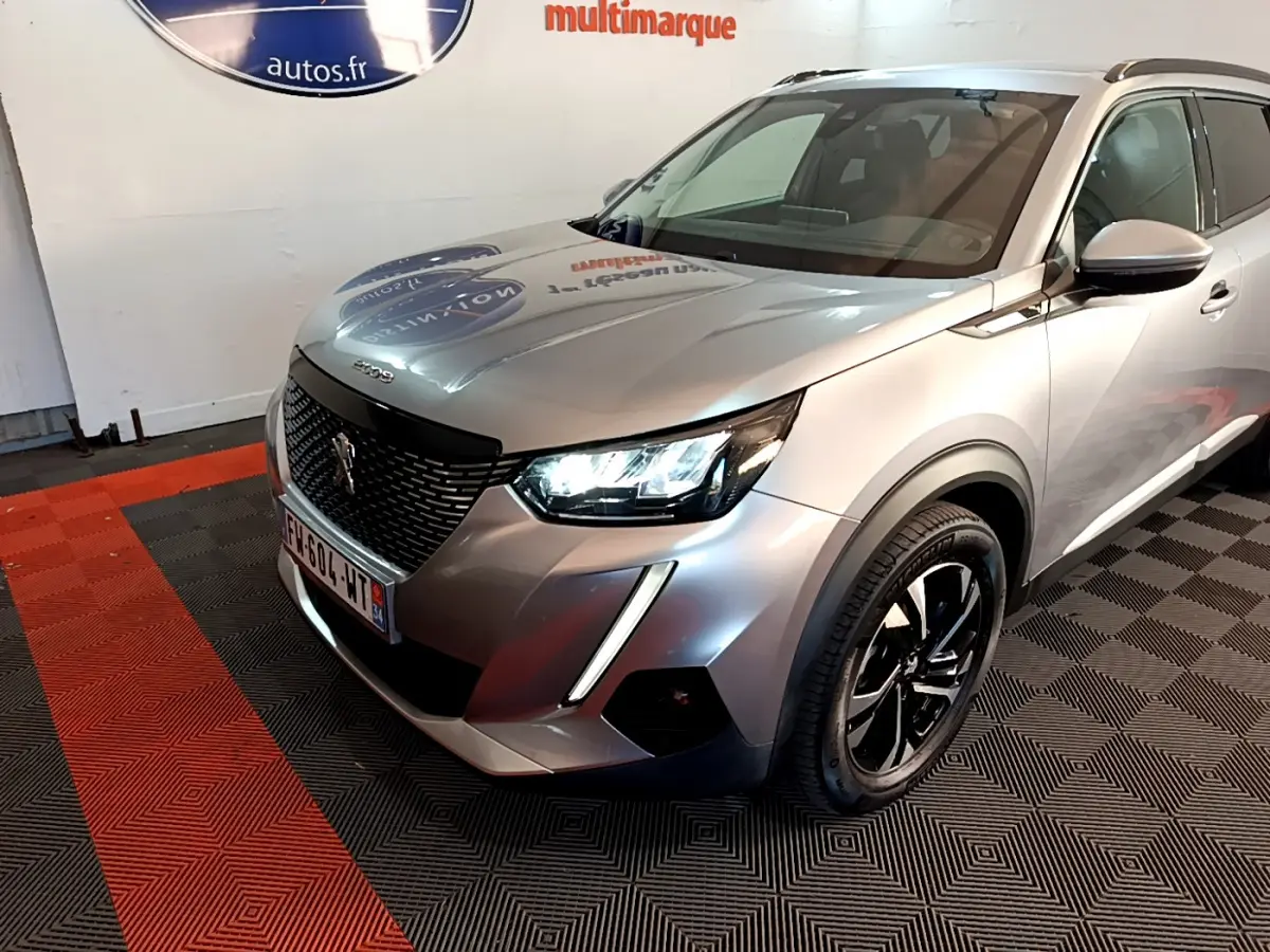 Peugeot 2008 gris clair en 3/4 avant droit, avec phares LED allumés et jantes noires distinctives.