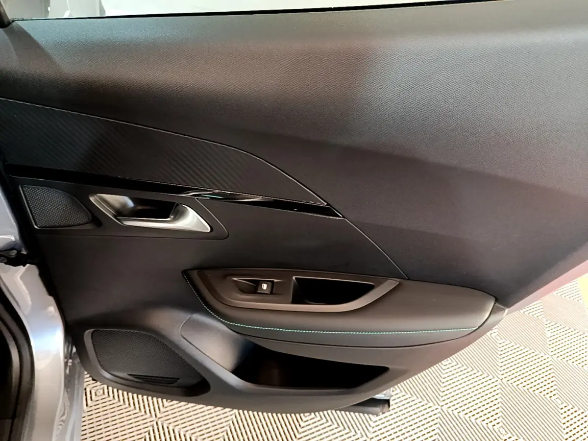 Porte côté gauche ouverte d'une Peugeot 2008 gris clair, avec garniture noire et surpiqûres bleues visibles.