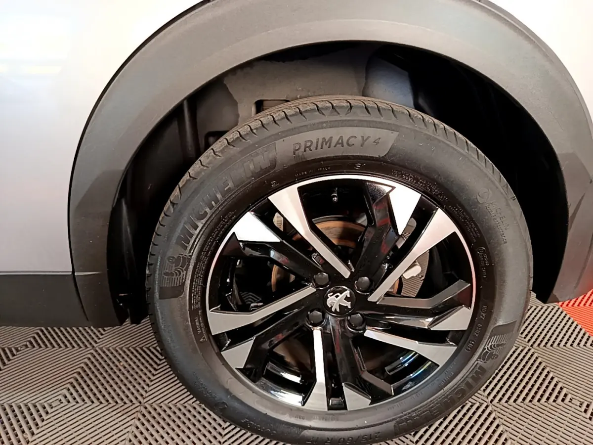 Gros plan sur la roue avant gauche d’un Peugeot 2008 gris clair, jante alliage noire et argentée avec logo lion central.