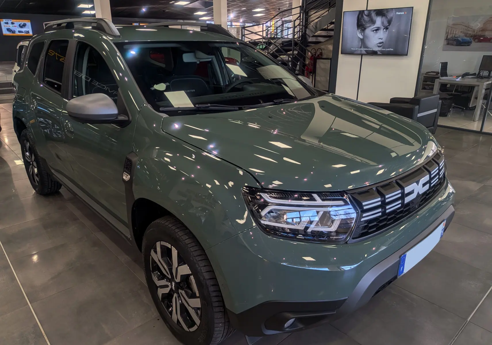 Vue 3/4 avant droite du Dacia Duster 2023 kaki lichen, avec calandre noire et jantes alliage bicolores en showroom.