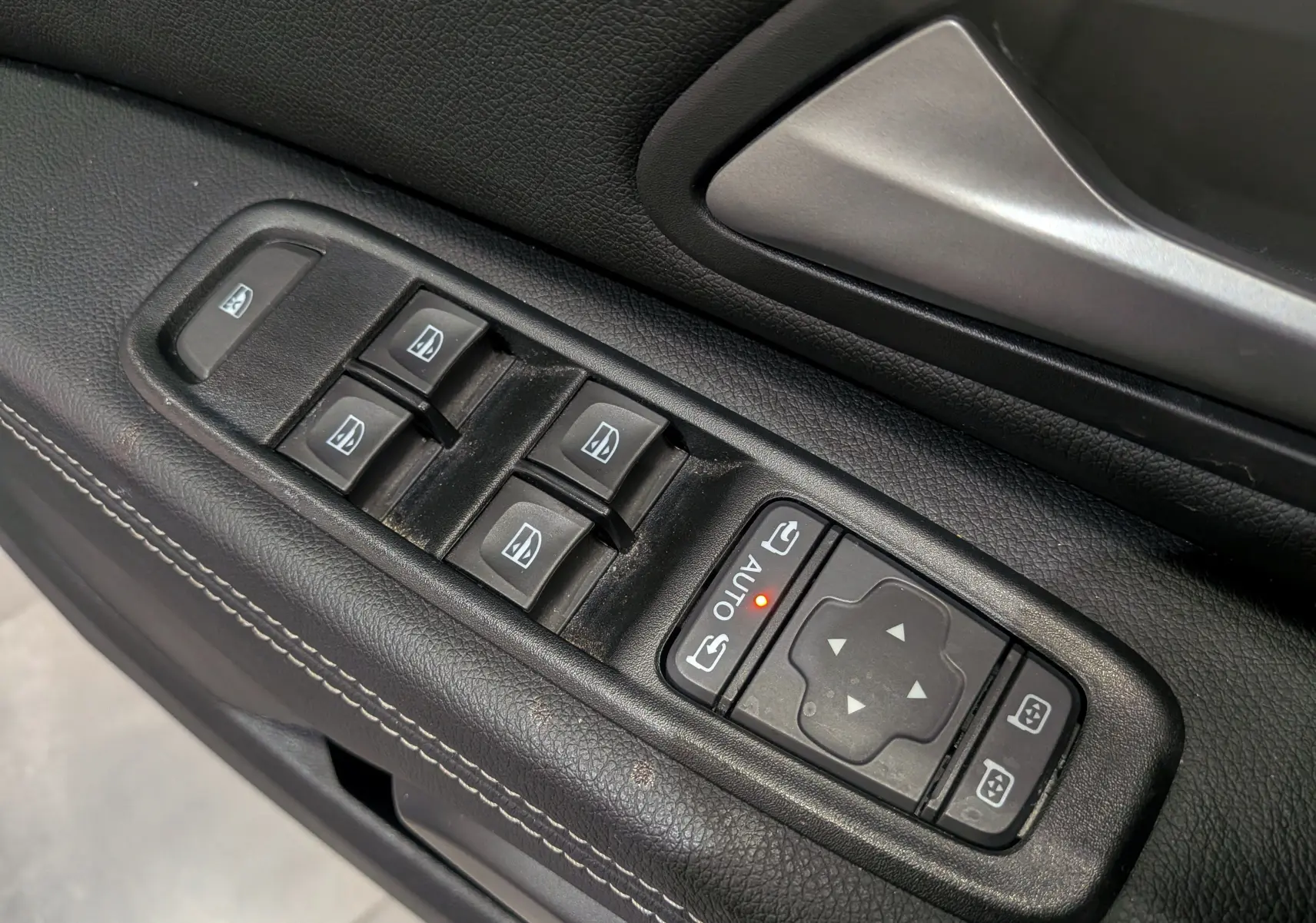 Gros plan sur les commandes de lève-vitres et réglage des rétroviseurs côté conducteur du Dacia Duster kaki 2023.