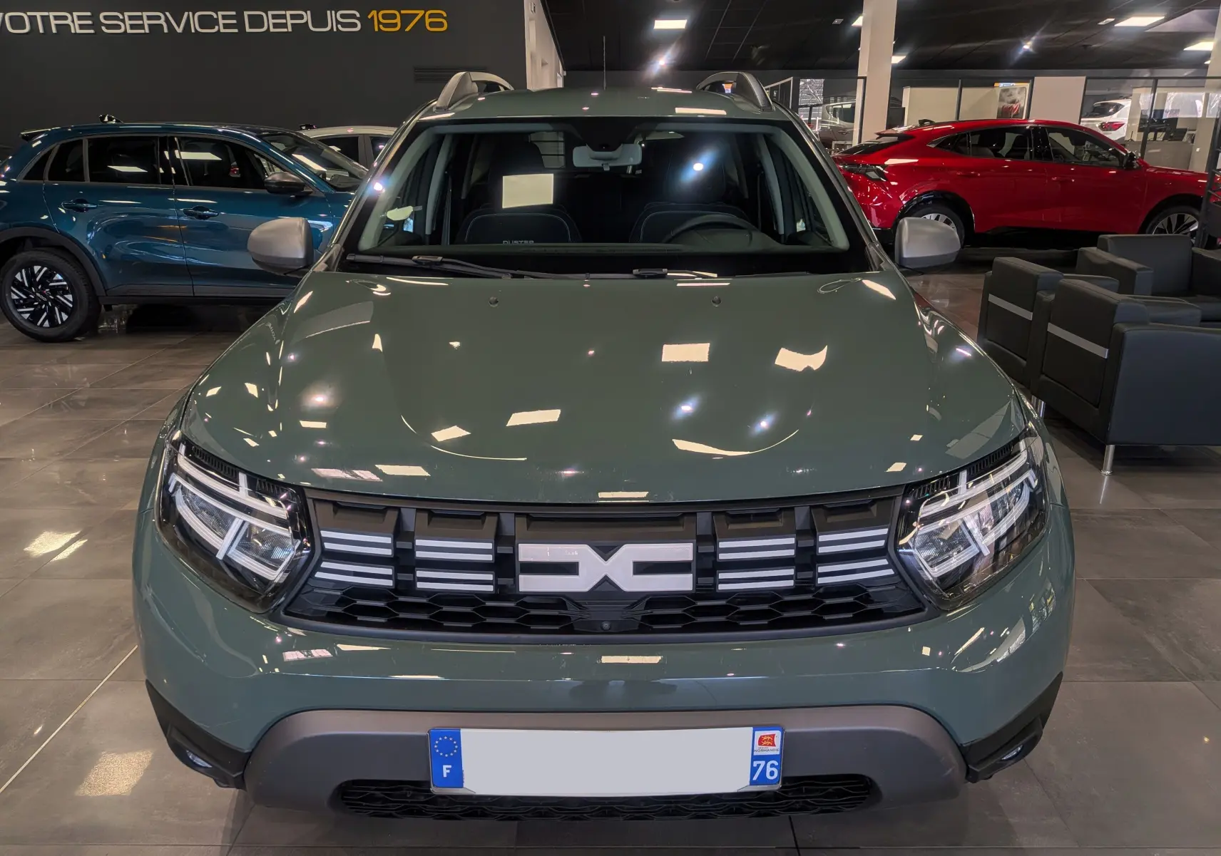 Vue frontale d'un Dacia Duster 2023 kaki lichen en showroom, avec calandre noire et détails chromés visibles.