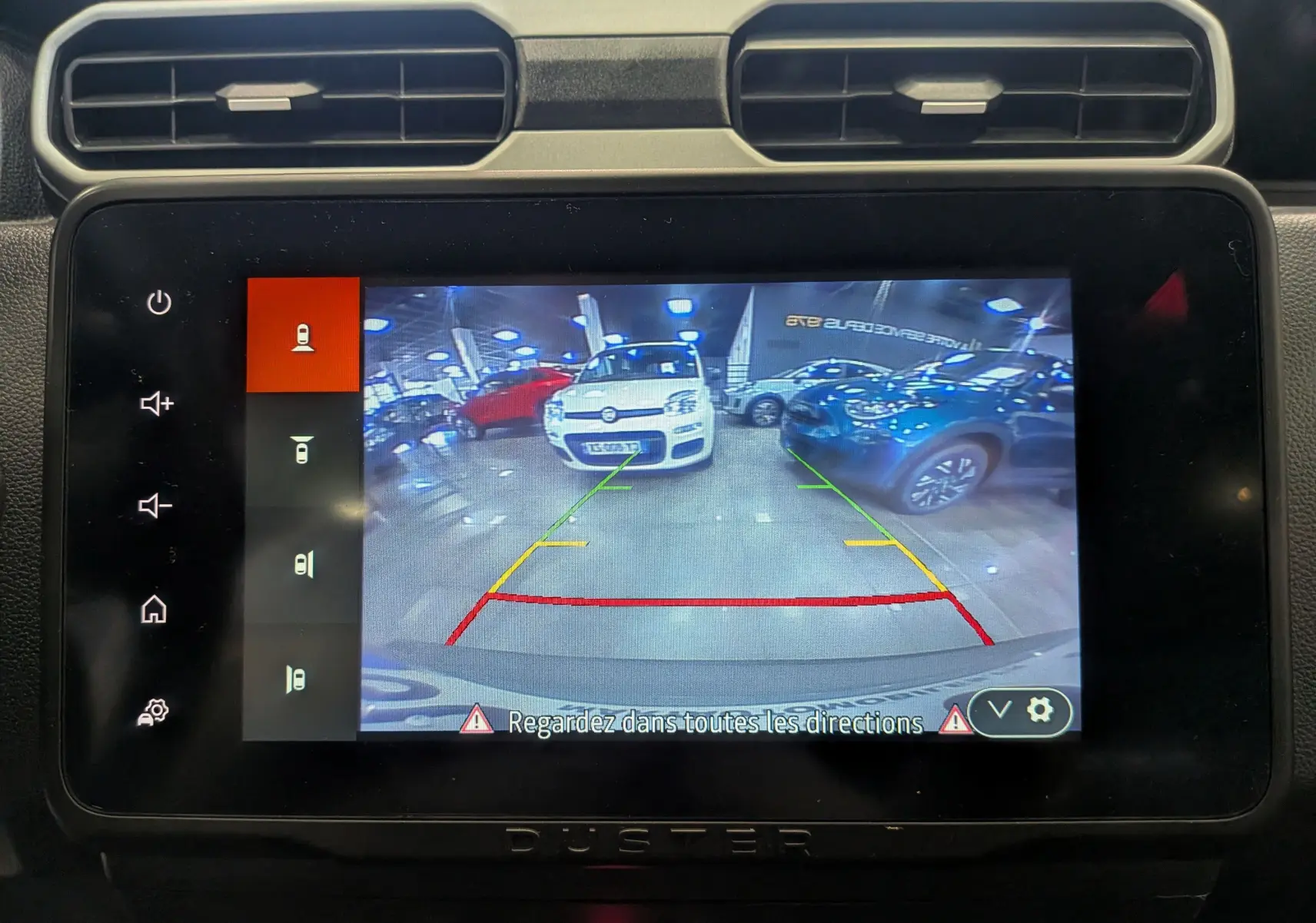 Écran tactile du Dacia Duster montrant la caméra de recul avec guidage coloré dans un garage lumineux.