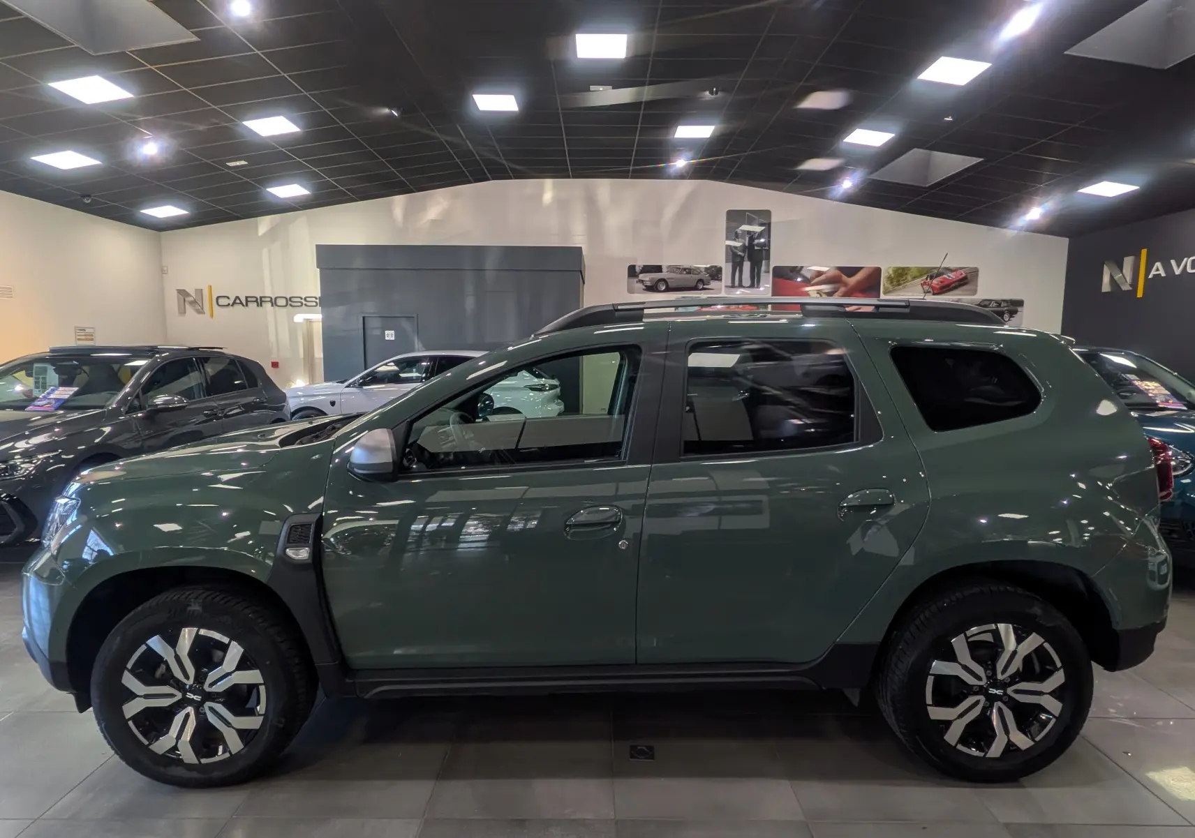 Vue de profil côté gauche du Dacia Duster 2023 kaki lichen avec jantes alliage bicolores en showroom.