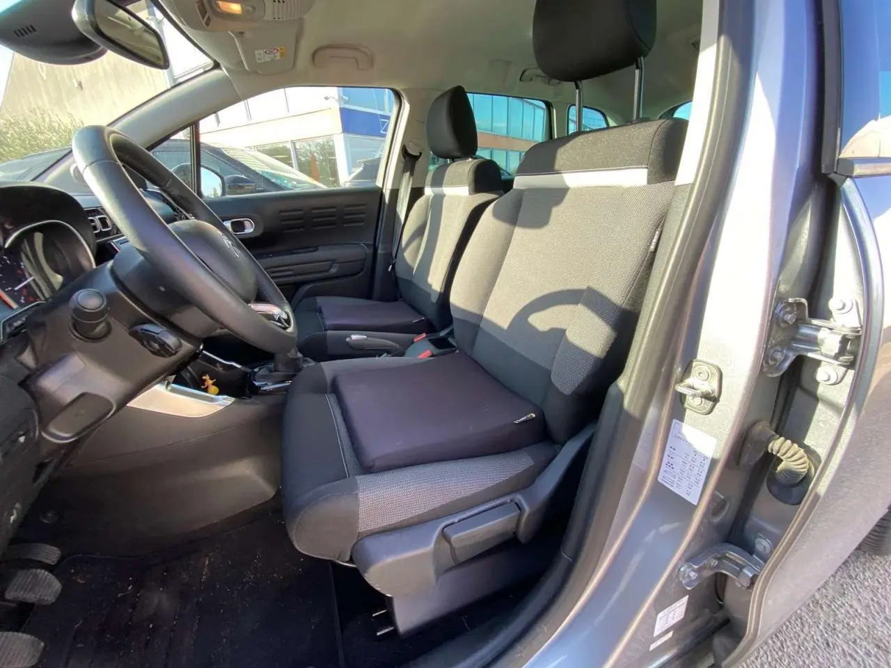 Vue intérieure côté conducteur du Citroën C3 Aircross gris foncé 2024, montrant les sièges avant et le volant.