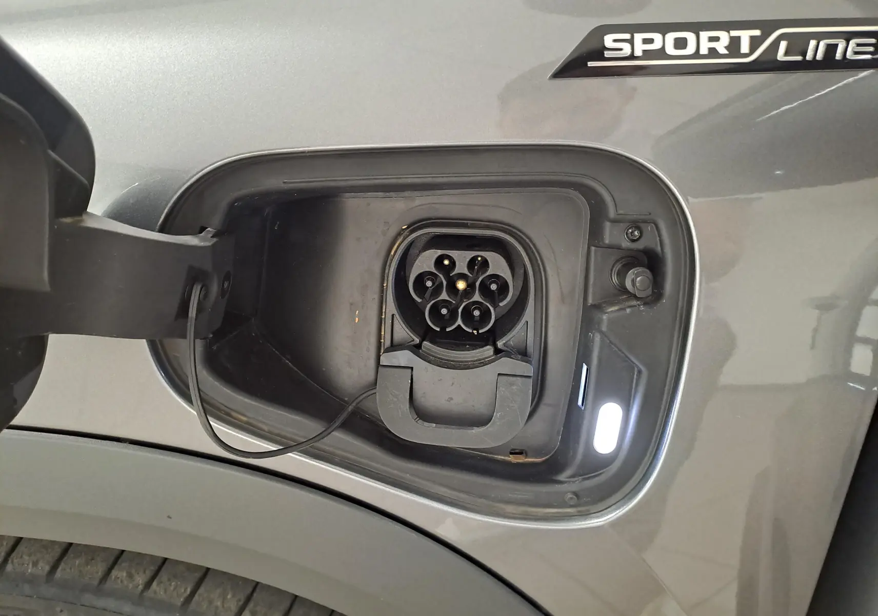 Prise de recharge ouverte côté gauche sur un Skoda Kodiaq Sportline gris graphite avec logo Sportline visible.