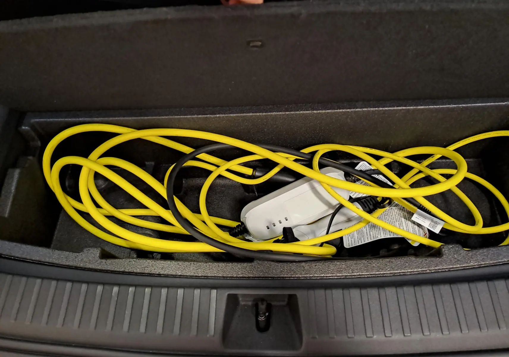 Coffre ouvert montrant le câble de recharge jaune et noir du Skoda Kodiaq hybride rechargeable, détail intérieur du coffre.