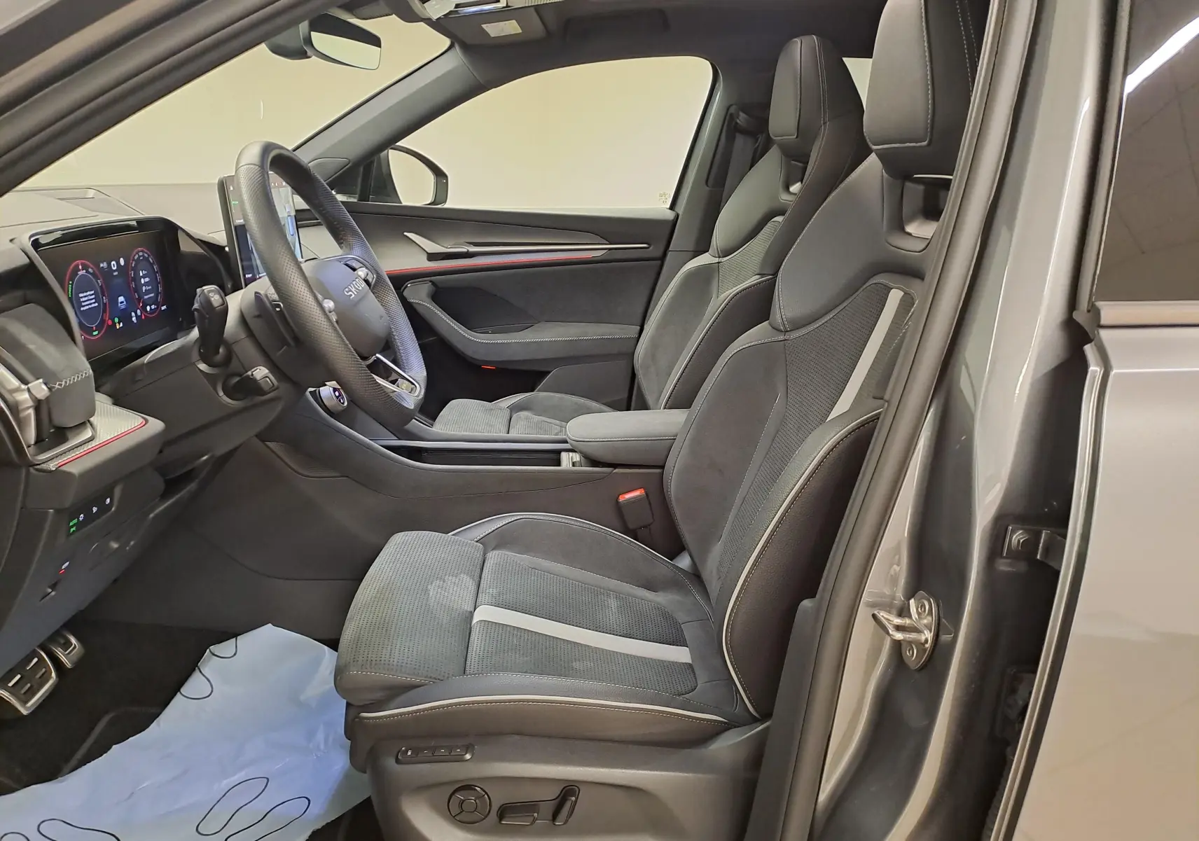 Vue intérieure côté conducteur du Skoda Kodiaq 2025 gris graphite, sièges sport noirs avec surpiqûres et tableau de bord digital.