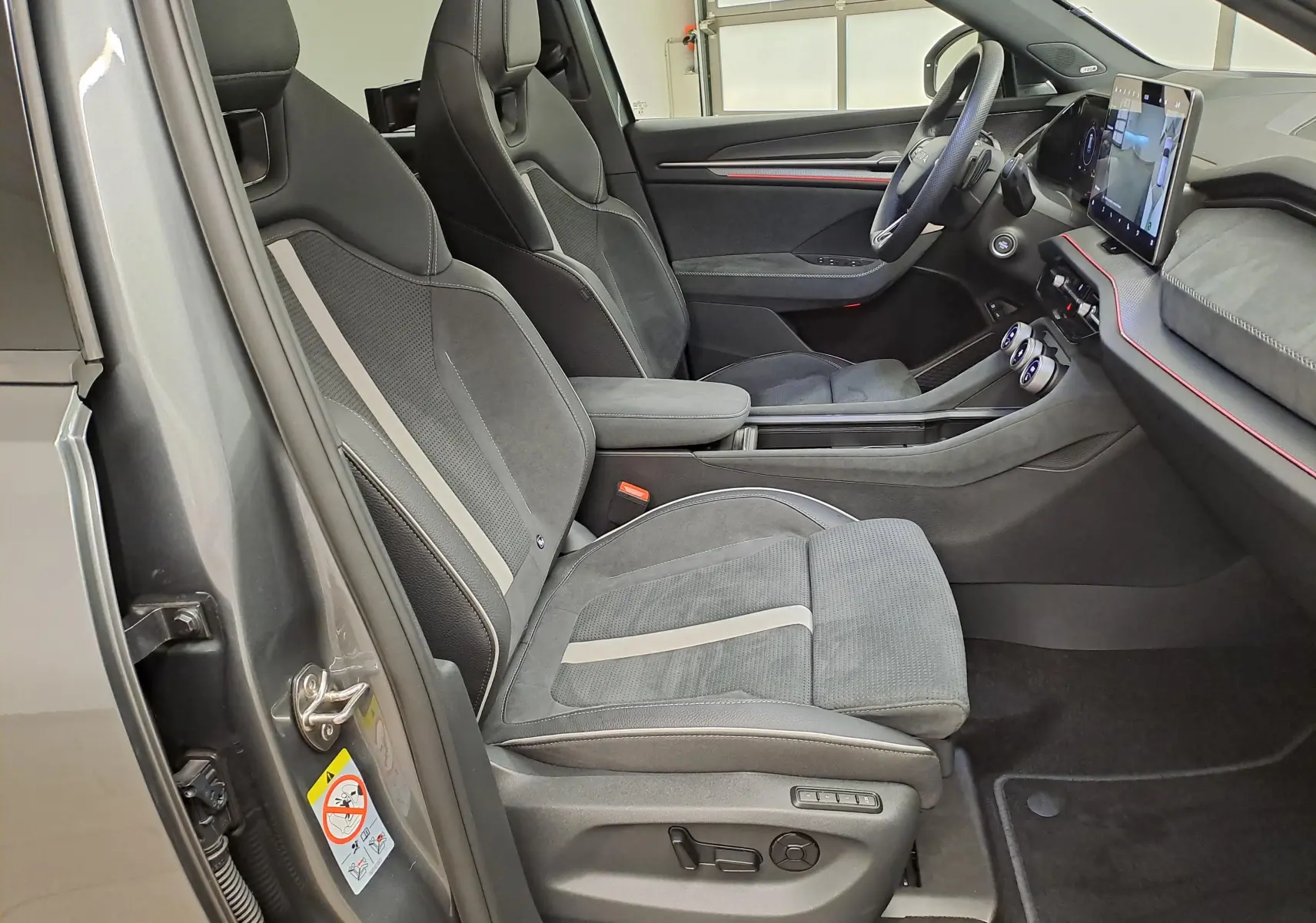 Vue intérieure côté gauche du Skoda Kodiaq gris graphite 2025, mettant en valeur les sièges sport et le tableau de bord moderne.