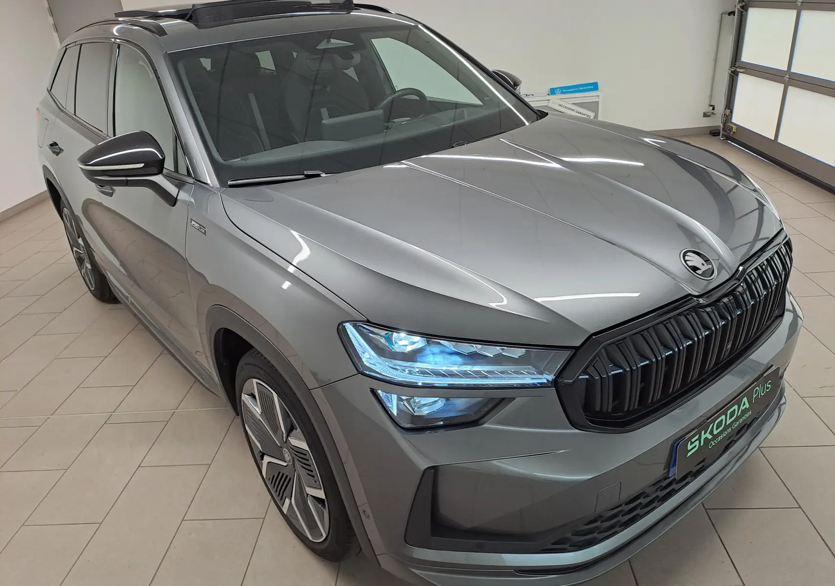 Vue 3/4 avant d'un Skoda Kodiaq gris graphite avec calandre noire et phares LED allumés en intérieur.