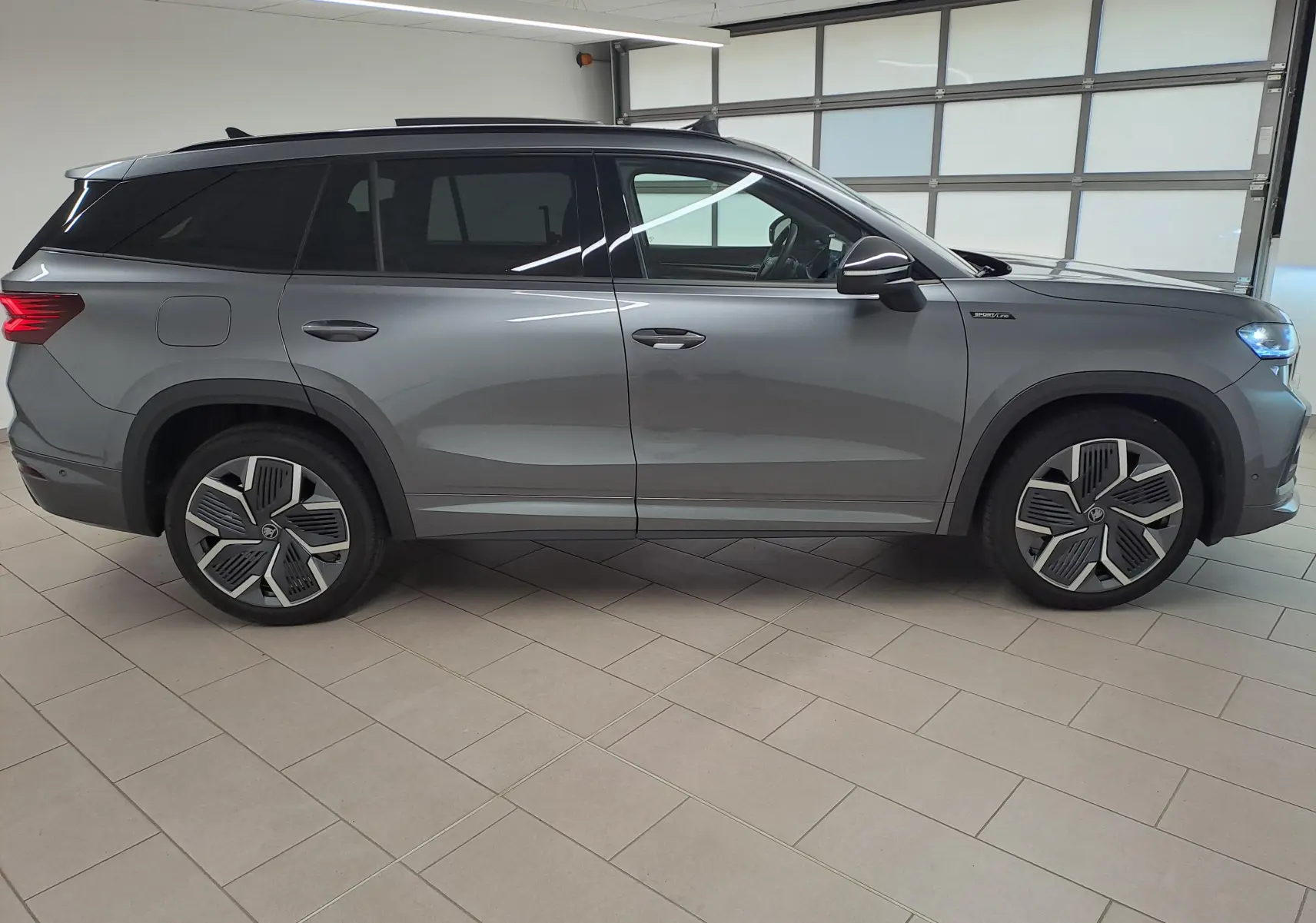 Vue de profil côté gauche d'un Skoda Kodiaq gris graphite avec jantes alliage 20'' et vitres teintées.