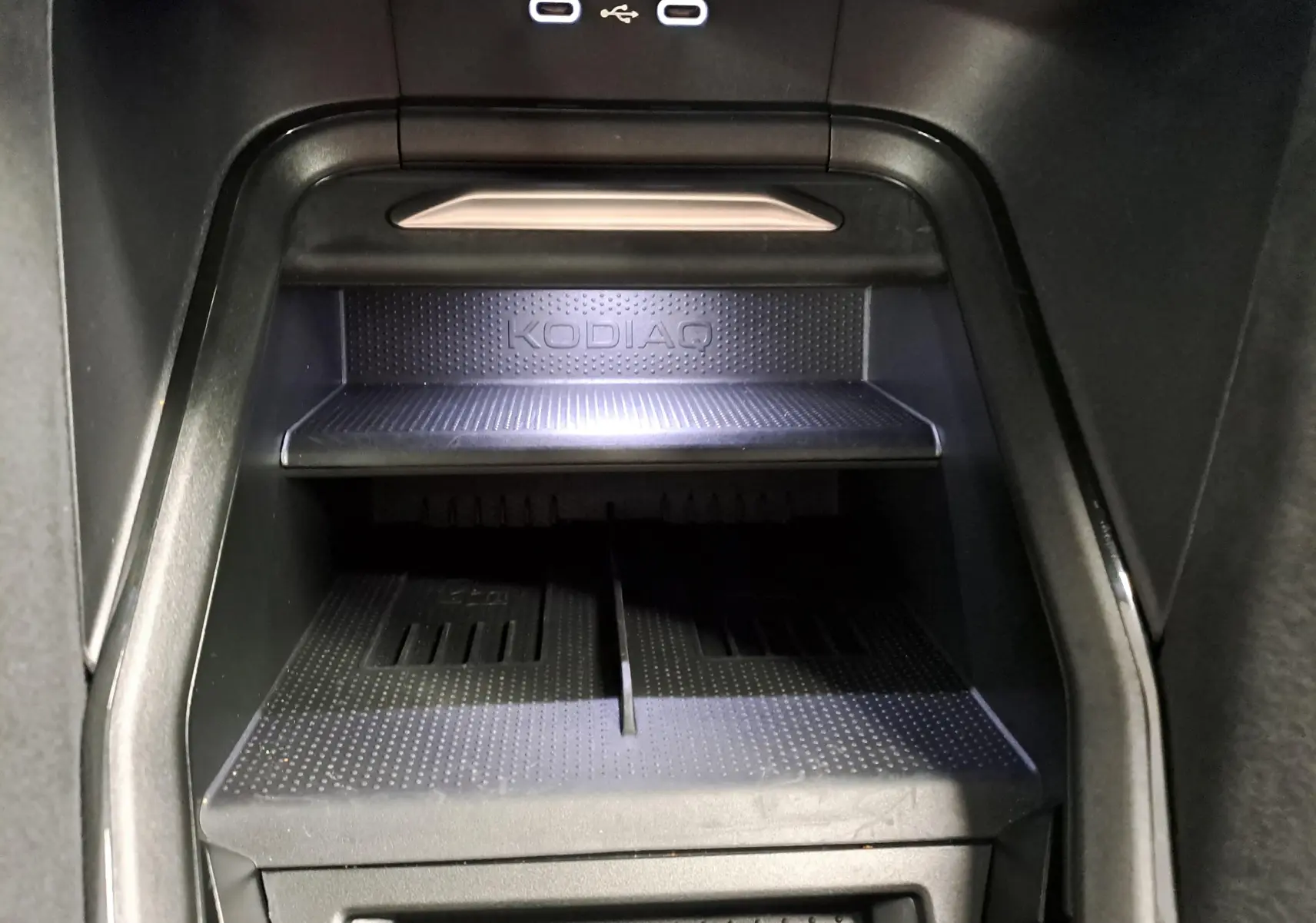 Gros plan intérieur sur le compartiment de rangement noir avec logo KODIAQ et ports USB éclairés du Skoda Kodiaq 2025.