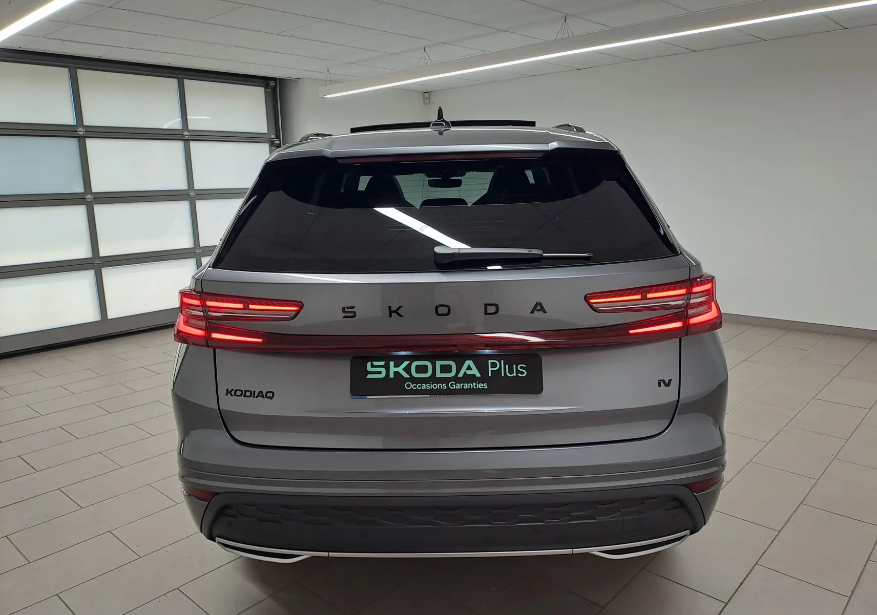 Vue arrière d'un Skoda Kodiaq gris graphite 2025 avec feux LED allumés et logo SKODA lumineux sur le hayon.
