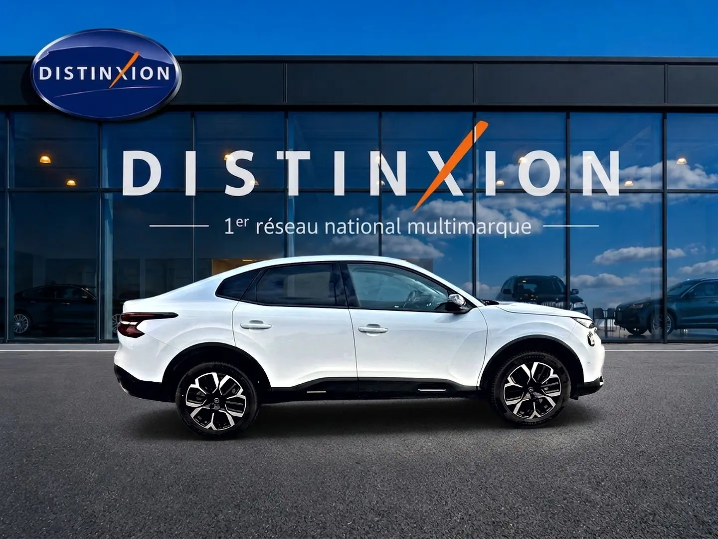 Profil droit de la Citroën C4 X blanche 2025 avec jantes alu noires et toit noir, devant une vitrine Distinxion.