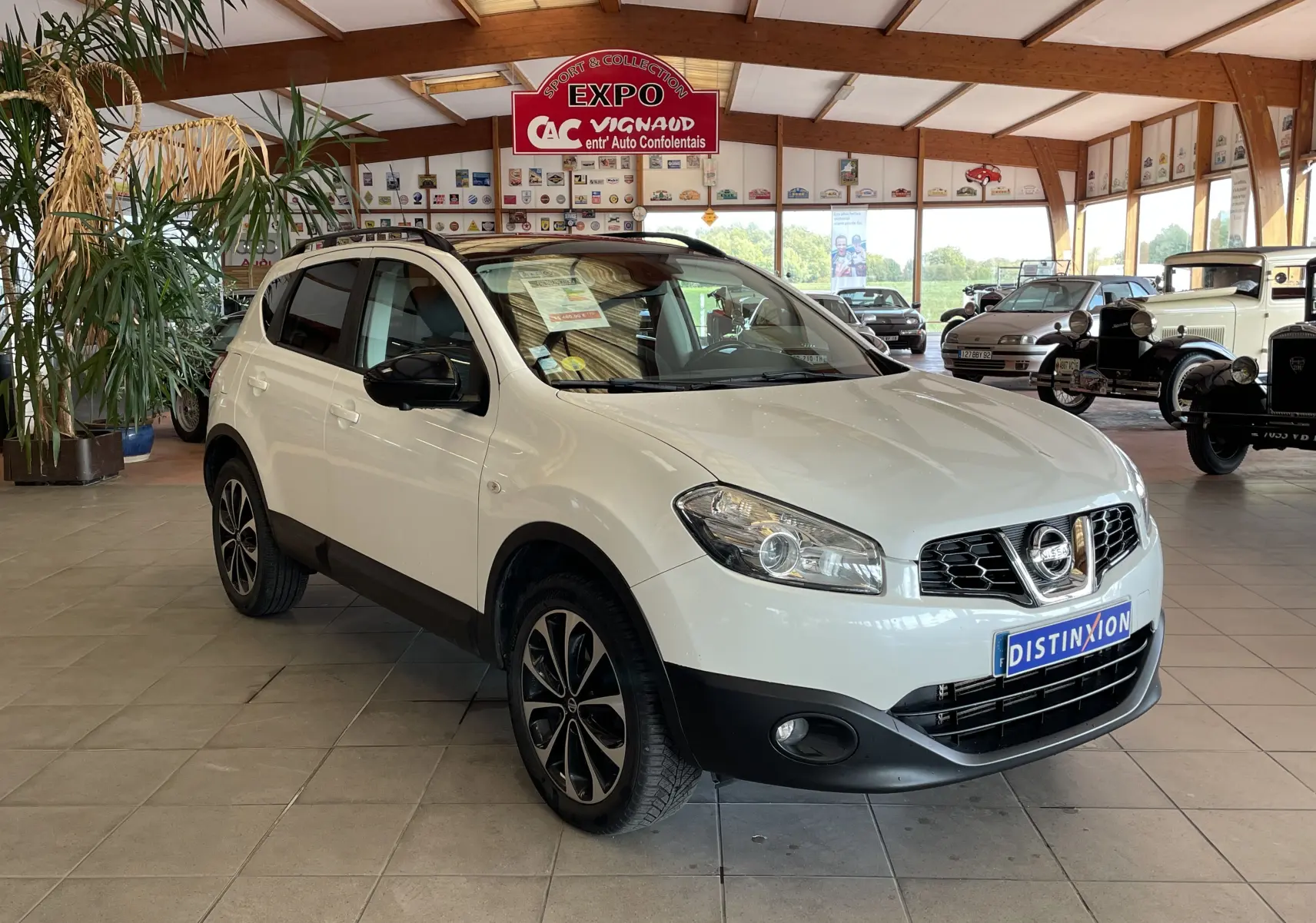 Nissan Qashqai blanc en 3/4 avant droit dans un showroom, avec jantes alliage et toit noir contrasté.